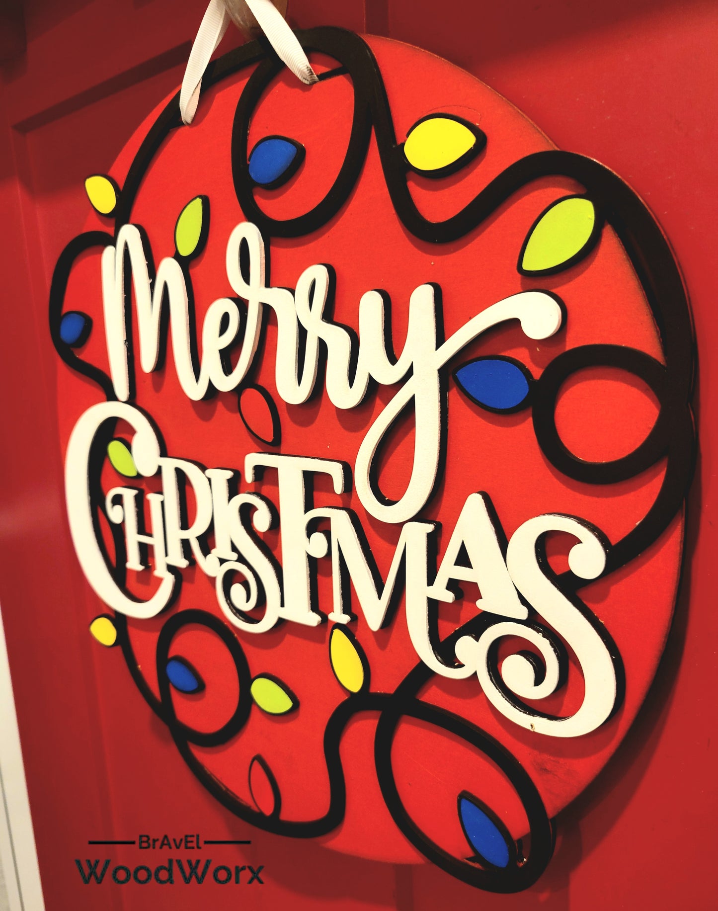 Layered wood Christmas door hanger featuring bold white lettering and festive light string design.