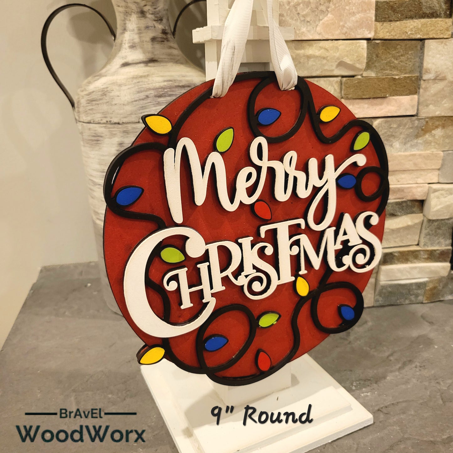 Holiday-themed round door sign that reads Merry Christmas with painted lights and ribbon hanger.