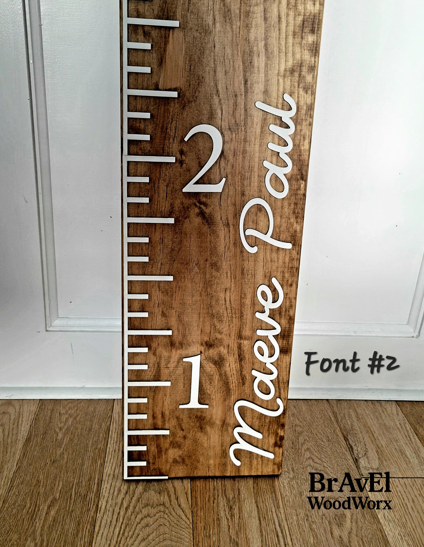 Wooden growth chart with ruler and 'Maeve Paul' engraving on a white background