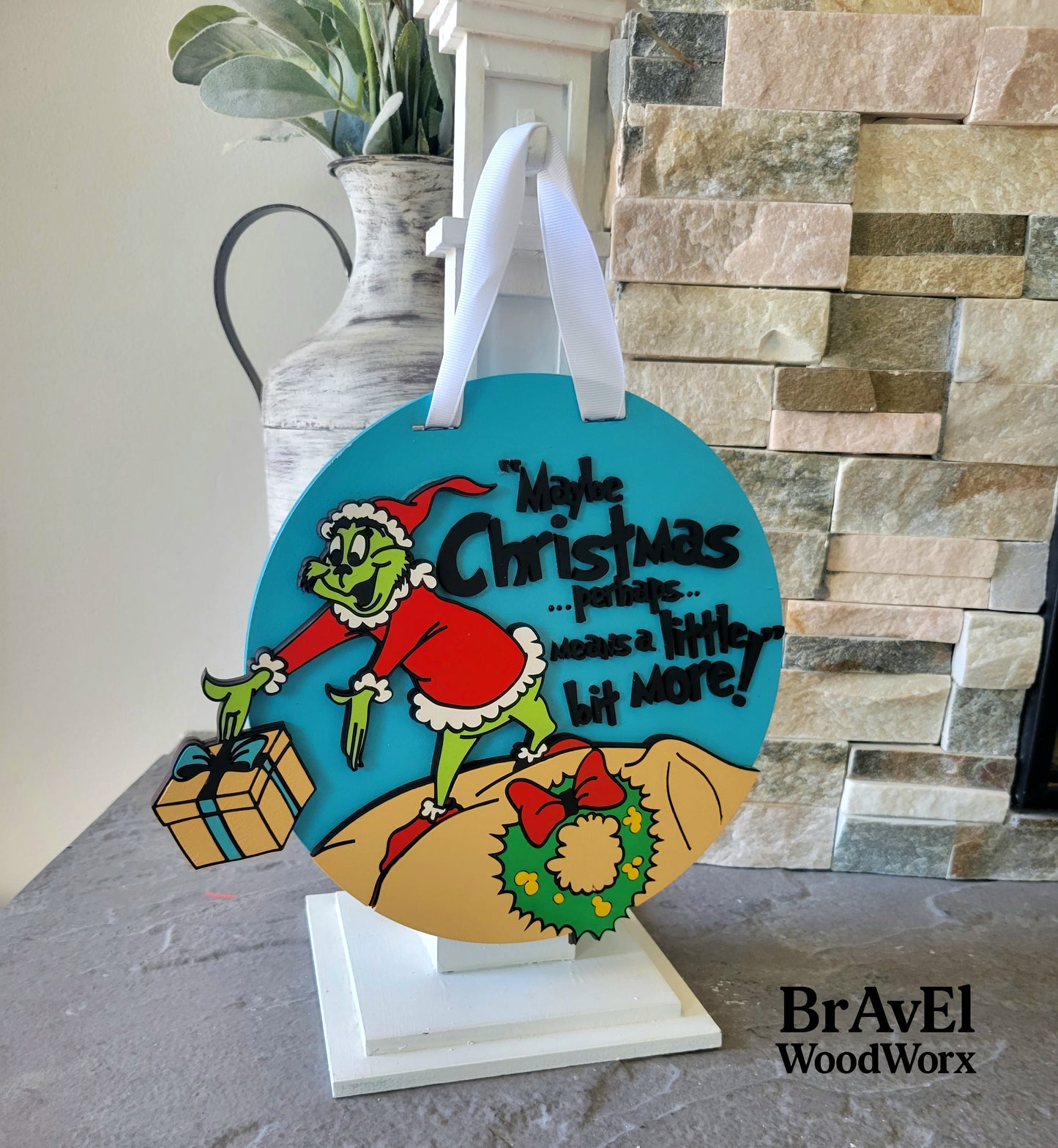 Decorative sign with Grinch design and text on a stand, featuring the brand 'BravEl WoodWorx'.