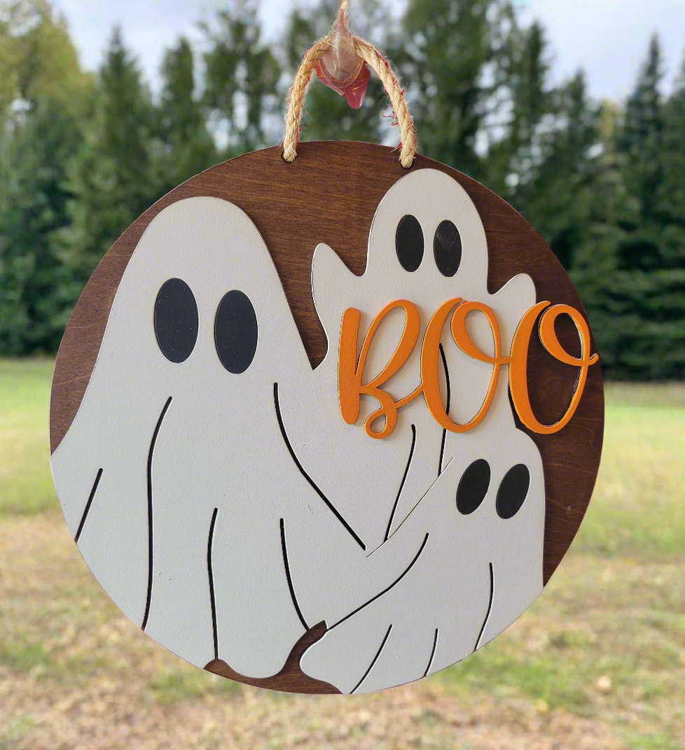 A round wood halloween sign with the word 'Boo' and decorative white ghost illustrations in the center, surrounded by a natural wood border.