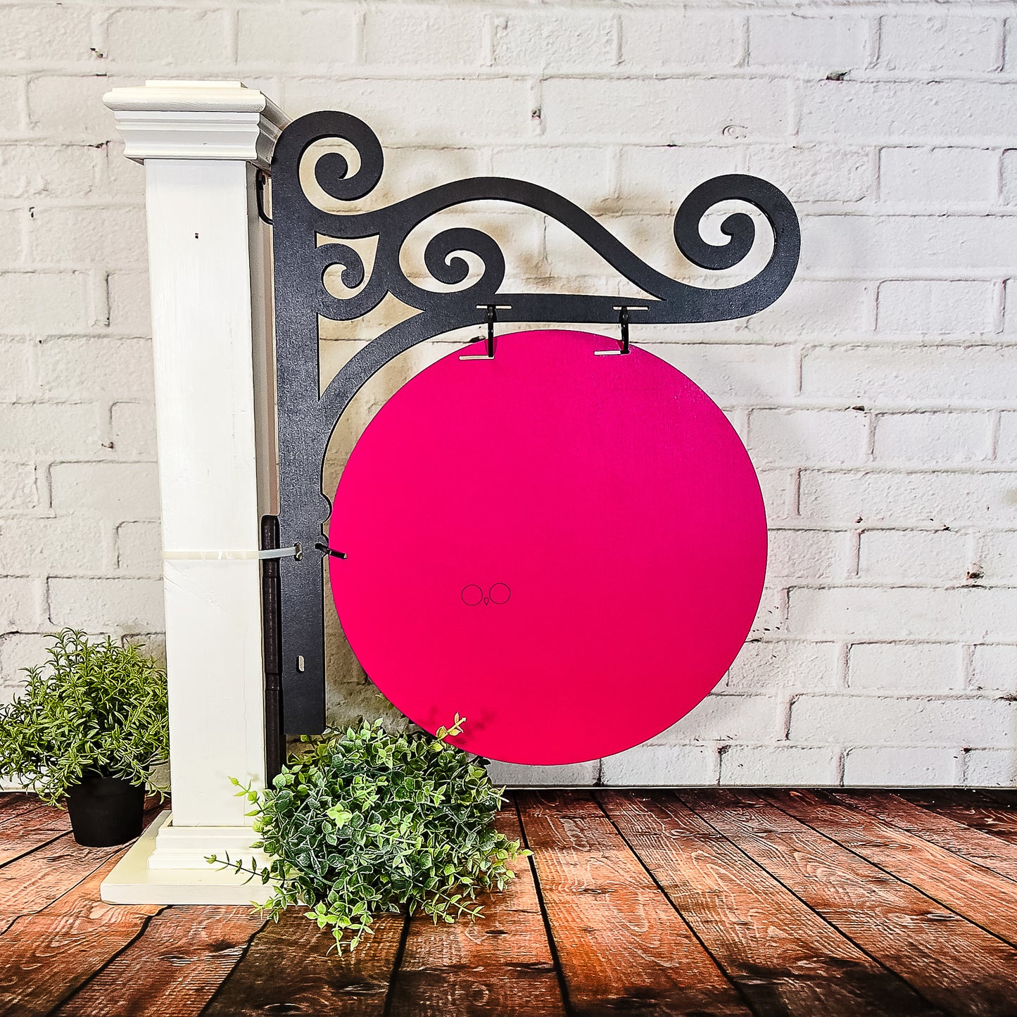 Decorative metal bracket with a pink circular sign against a white brick wall.