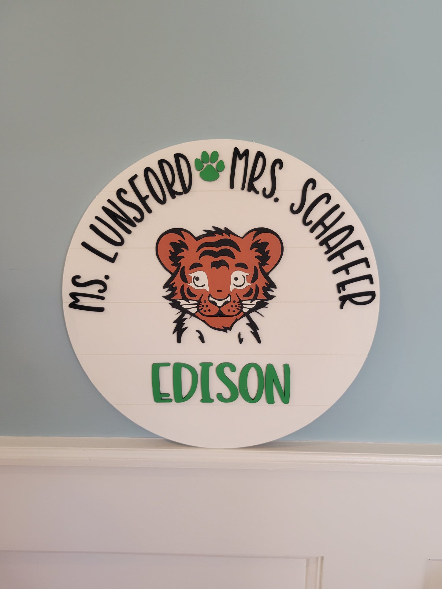 Circular name tag with a tiger illustration and text on a light blue wall.
