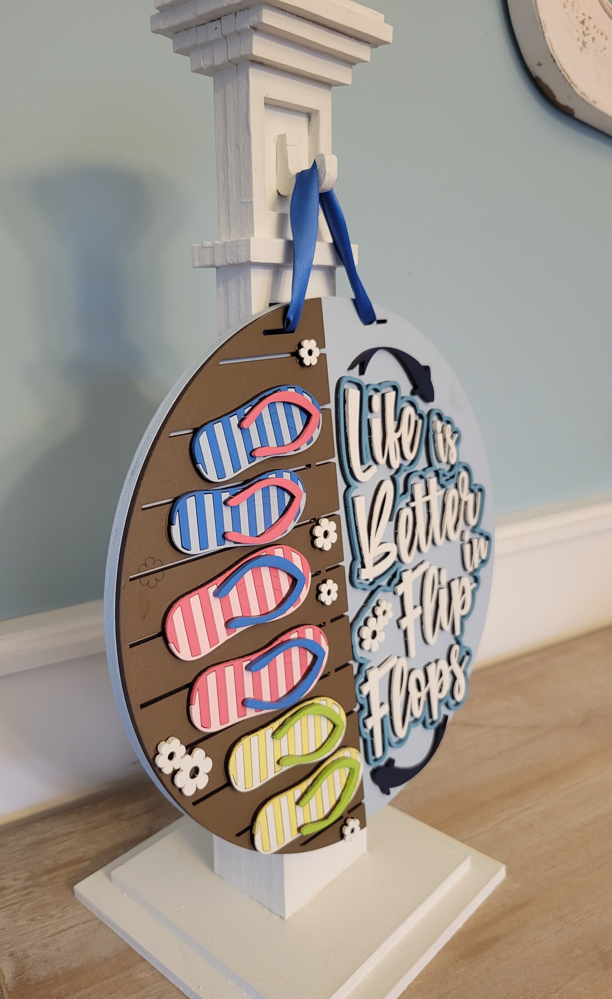 A rectangular wooden sign with a coastal vibe, featuring the text "Life is Better in Flip Flops" written in a playful, beach-inspired font. The background is painted in soft turquoise with a weathered wood texture, accented by illustrations of flip flops and small seashells. Perfect for beach houses, patios, or summer decor. White post side