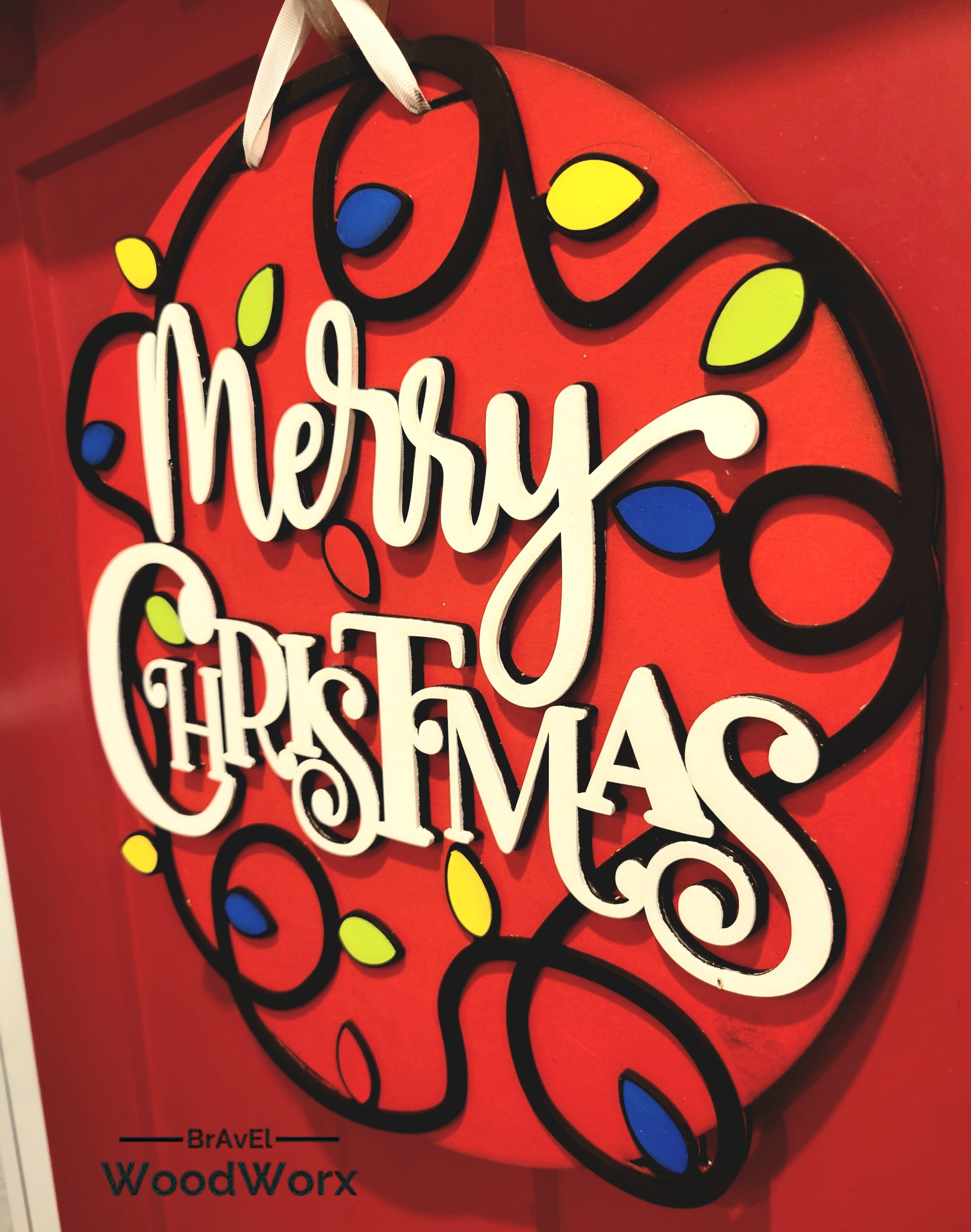 Layered wood Christmas door hanger featuring bold white lettering and festive light string design.