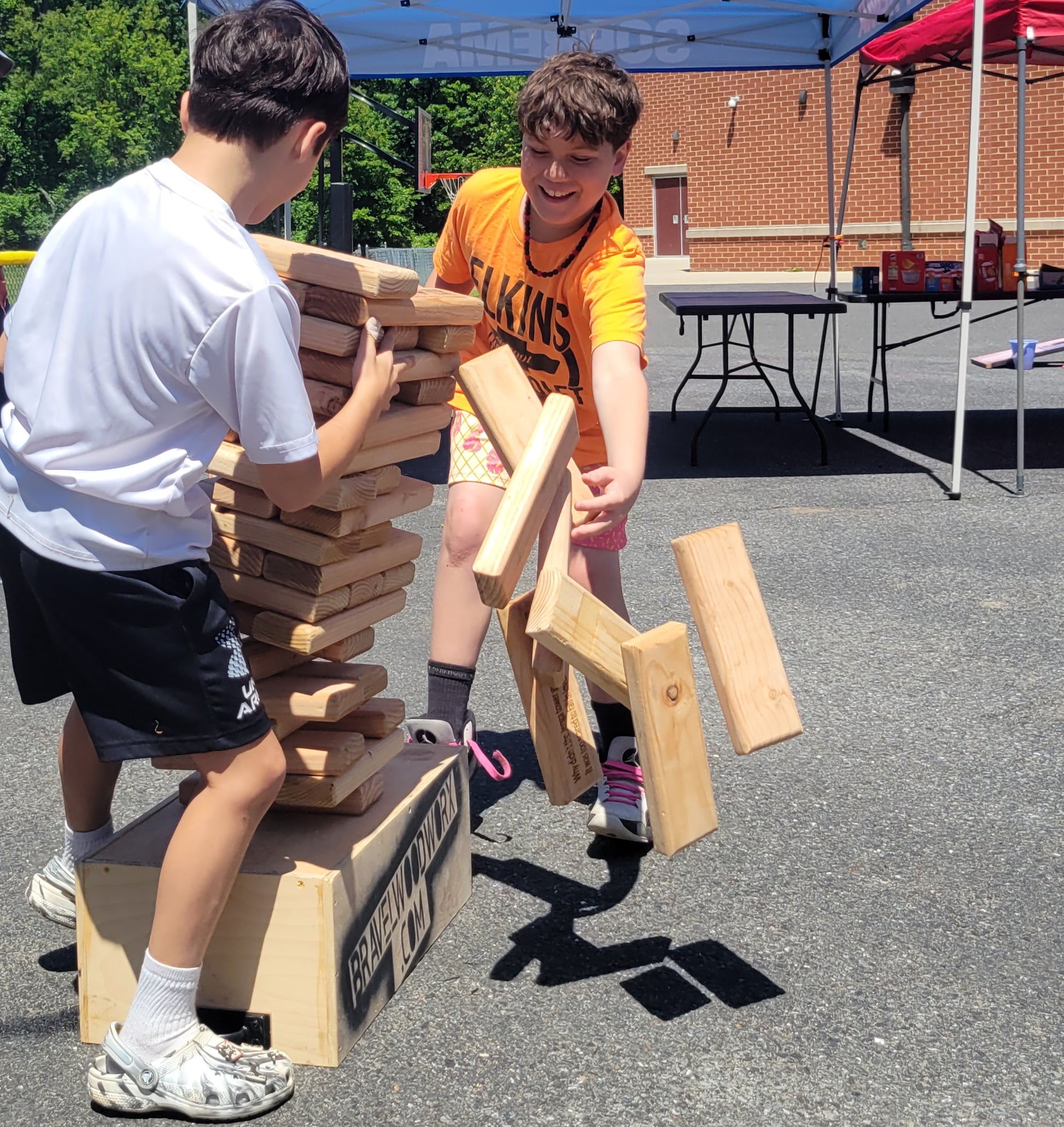 Two children playing with a large wooden block game outdoors.