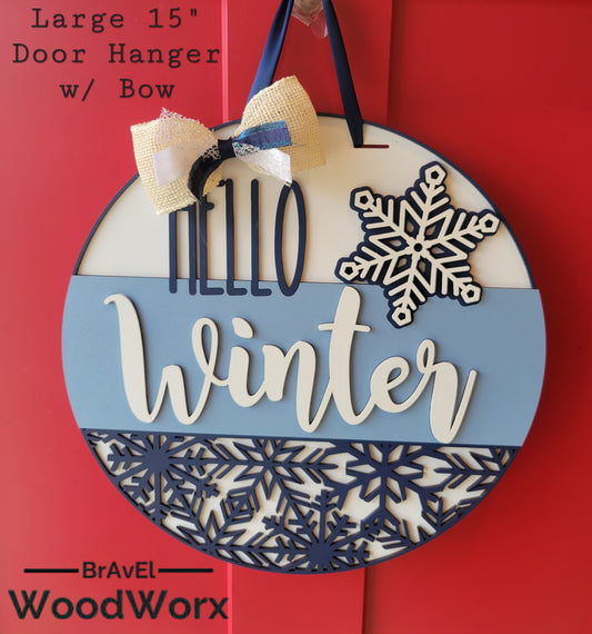 A round "Hello Winter" snowflake door hanger, crafted from wood, featuring intricate laser-cut snowflake designs and the text "Hello Winter" in elegant script. The sign is painted in a festive color palette, perfect for adding a seasonal touch to your home's decor. Hanging on a front door, it embodies warmth and winter charm
