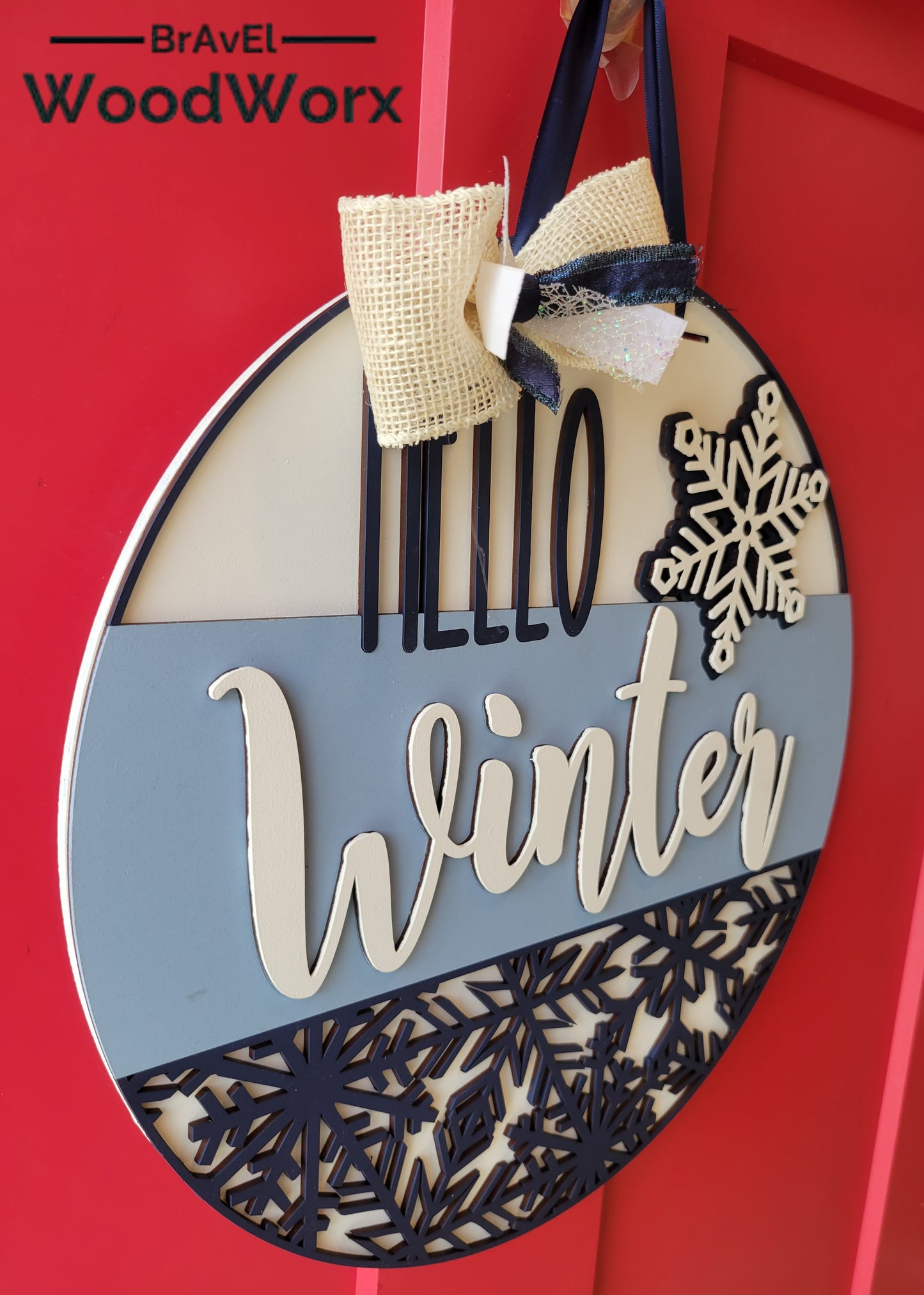 A round "Hello Winter" snowflake door hanger, crafted from wood, featuring intricate laser-cut snowflake designs and the text "Hello Winter" in elegant script. The sign is painted in a festive color palette, perfect for adding a seasonal touch to your home's decor. Hanging on a front door, it embodies warmth and winter charm side view