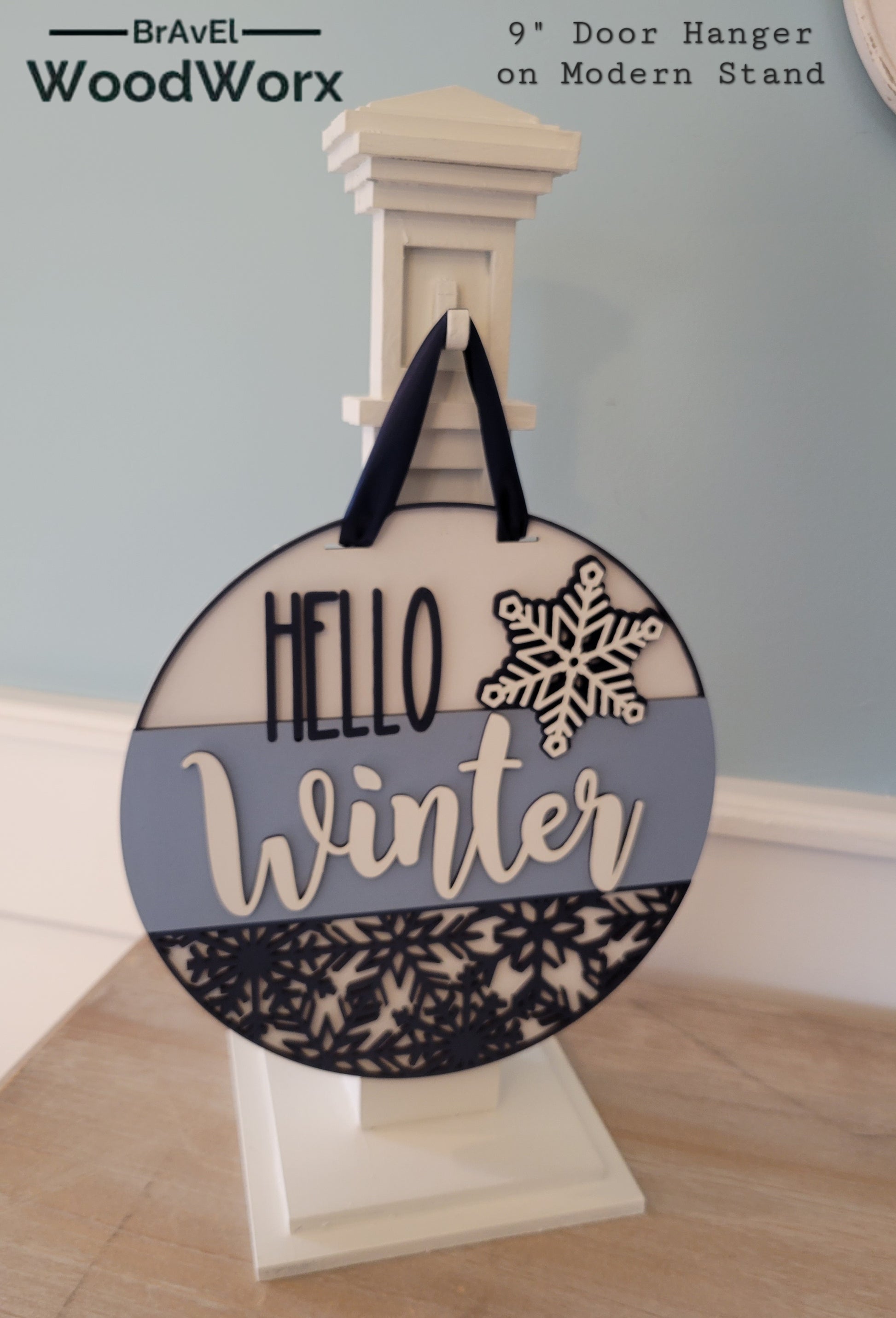 A wooden "Hello Winter" snowflake shelf stand featuring an intricate laser-cut snowflake design and the words "Hello Winter" in stylish script. Painted in a festive winter-themed color palette, it sits beautifully on a mantel or shelf, adding a cozy seasonal touch to your home decor.