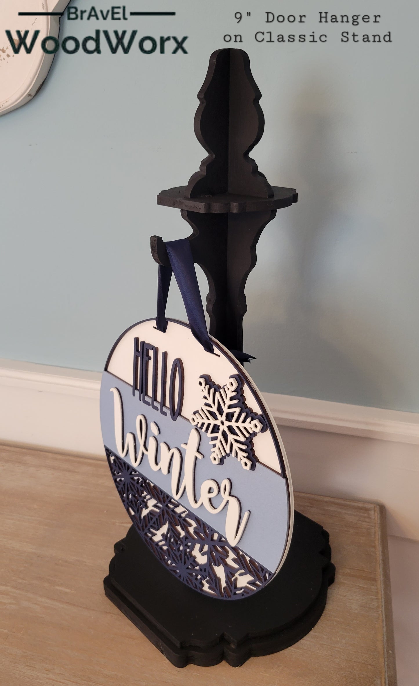 A wooden "Hello Winter" snowflake shelf stand featuring an intricate laser-cut snowflake design and the words "Hello Winter" in stylish script. Painted in a festive winter-themed color palette, it sits beautifully on a mantel or shelf, adding a cozy seasonal touch to your home decor. classic stand side view