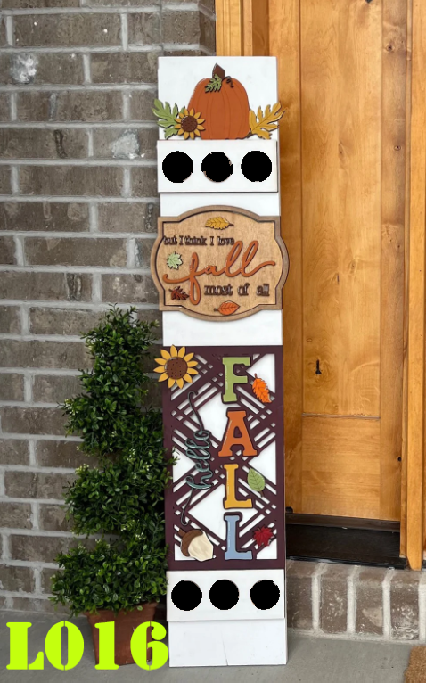 Decorative fall-themed sign with pumpkins, leaves, and sunflowers against a brick wall.