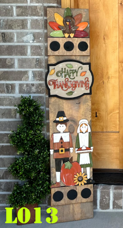 Decorative Thanksgiving sign with pilgrims, a turkey, and 'Happy Thanksgiving' text on a wooden board against a brick wall.