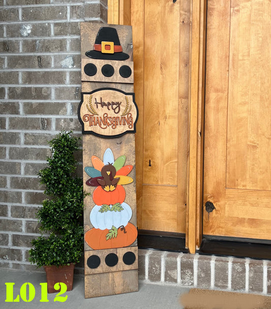 Wooden Thanksgiving sign with pilgrim hat, turkey, and pumpkin design against a brick wall.