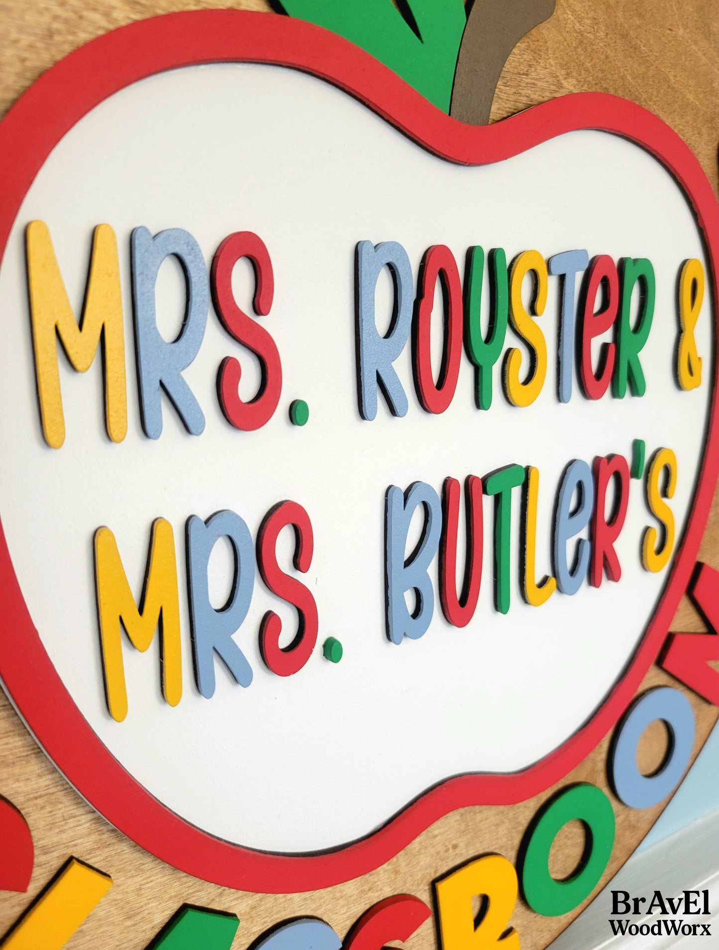 Colorful apple-shaped sign with 'Mrs. Royster & Mrs. Butler's' text on a wooden background