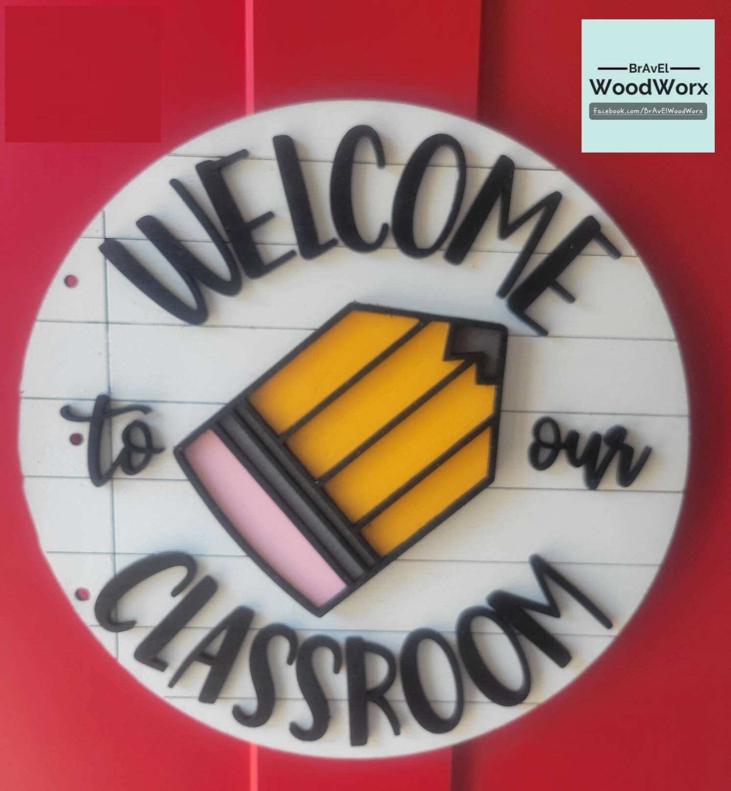 A round, wooden sign with a white background, featuring the text 'Welcome to our CLASSROOM' in bold black letters, accompanied by an illustration of a pencil and yellow accents. The sign is designed to be wall or door mounted.