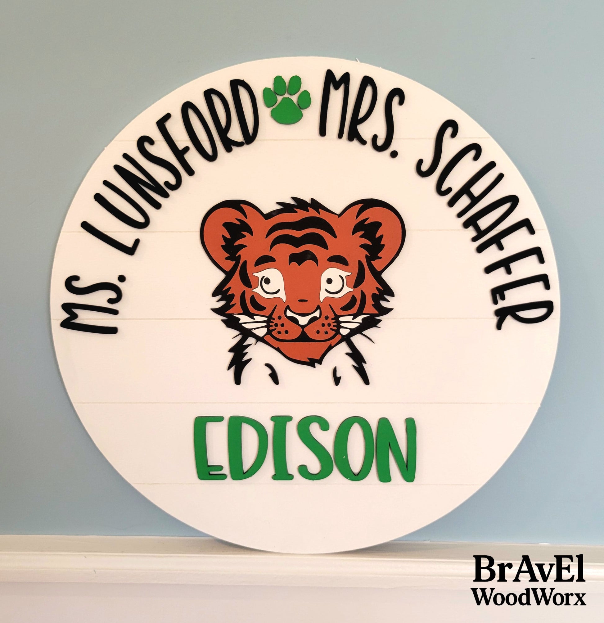 Circular wooden sign with tiger illustration and text on a gray background, featuring the brand 'BravEl WoodWorx'.