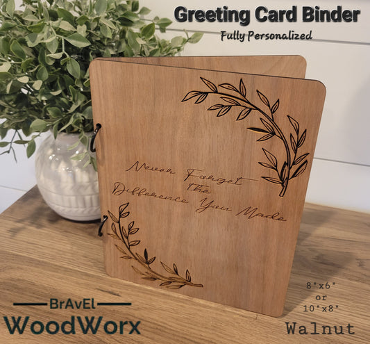 A personalized walnut greeting card binder with an engraved floral design on the cover, resting on a wooden surface with a white pen and ink nearby.