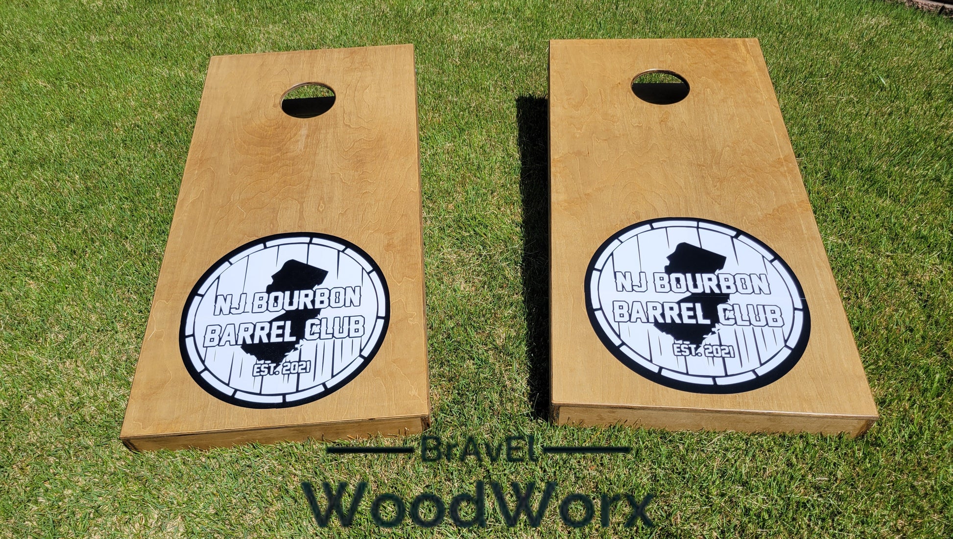Two wooden cornhole boards with a monogram and the text 'Middourbon Barrel Club' engraved on them, placed on grass with the brand 'BrAvEl WoodWorx' visible.