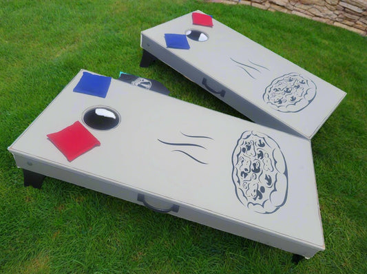 Two wooden cornhole boards with a design resembling a pizza on one of them, placed on grass with a background of a yard.