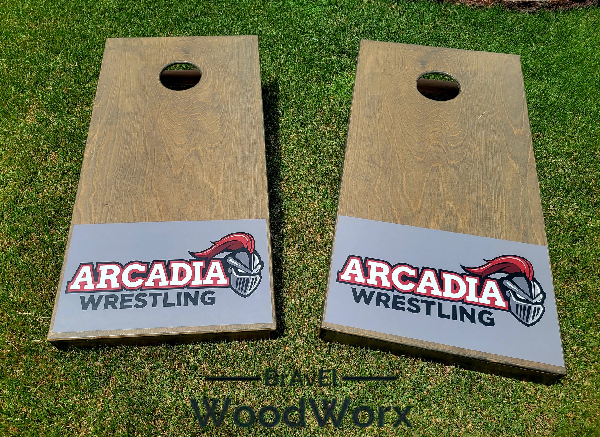 Two wooden cornhole boards with 'Arcadia Wrestling' branding on a grassy background.