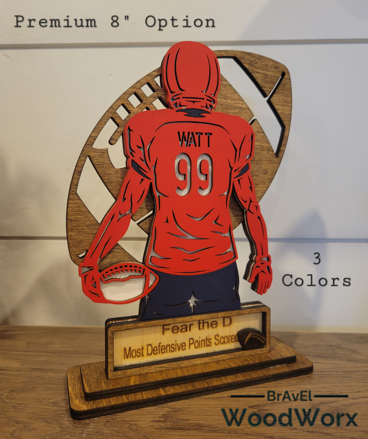 A wooden trophy featuring a customizable football player figure in a red jersey with the number 99, accompanied by a trophy stand. The text 'Premium 8 Option' and 'Fear The D' are visible, along with the brand name 'BrAvEl'.