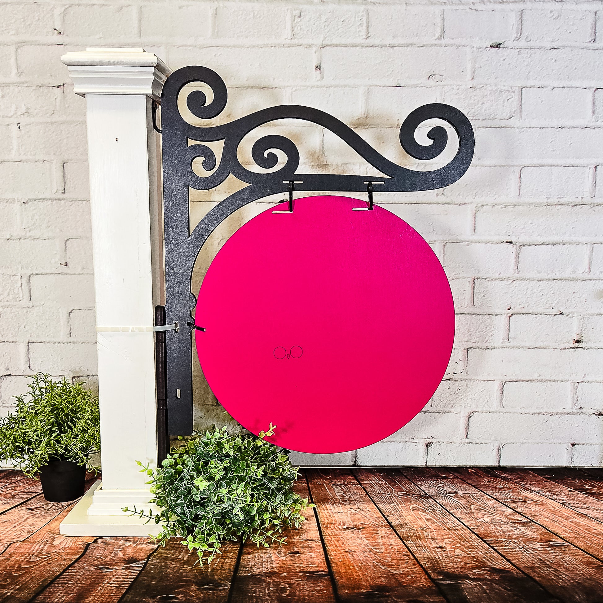 Decorative metal bracket with a pink circular sign against a white brick wall.
