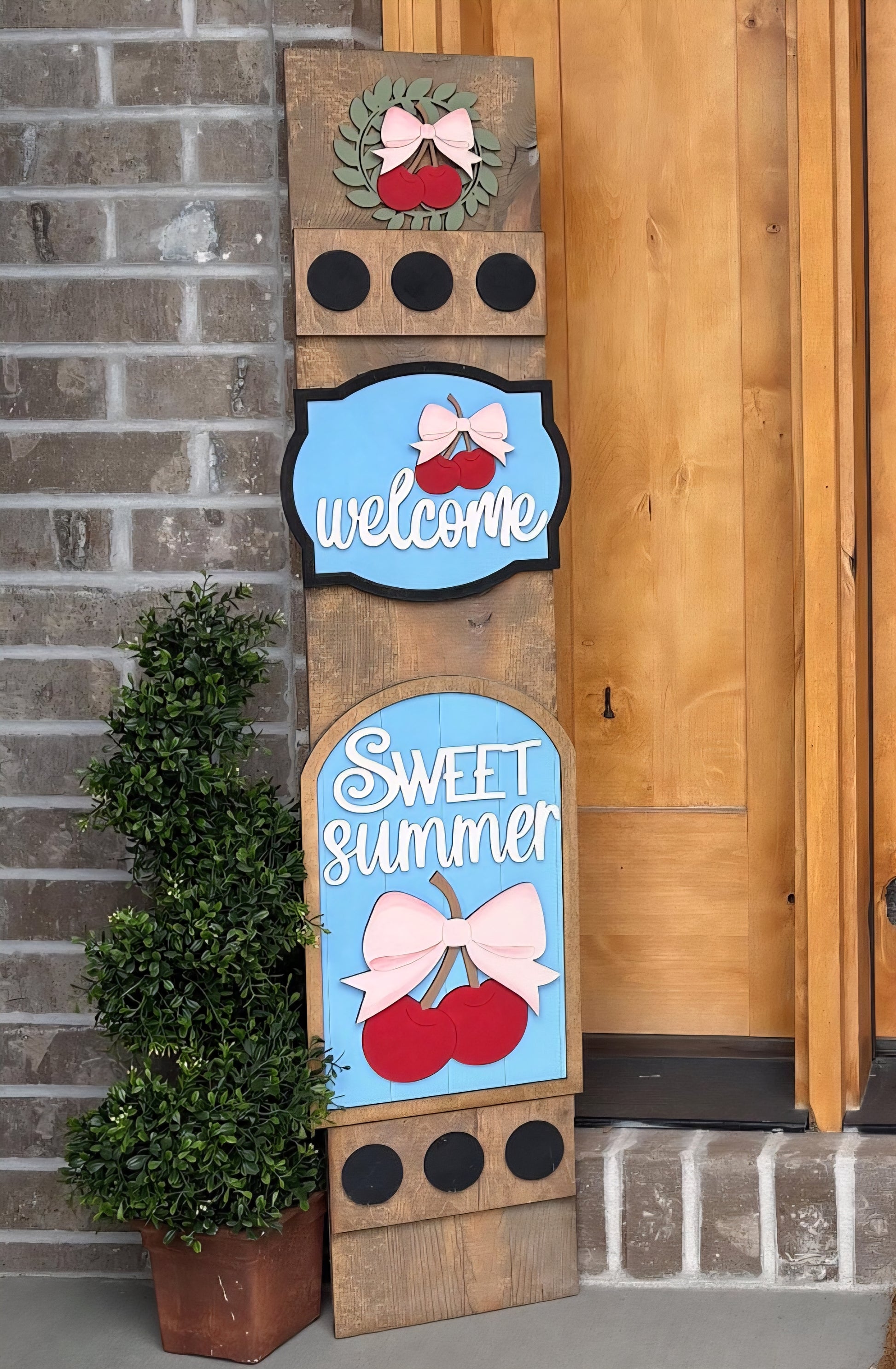 Decorative wooden sign with 'welcome' and 'sweet summer' text against a brick wall.