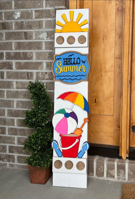 Decorative sign with summer elements like a sun, beach ball, and umbrella against a brick wall.