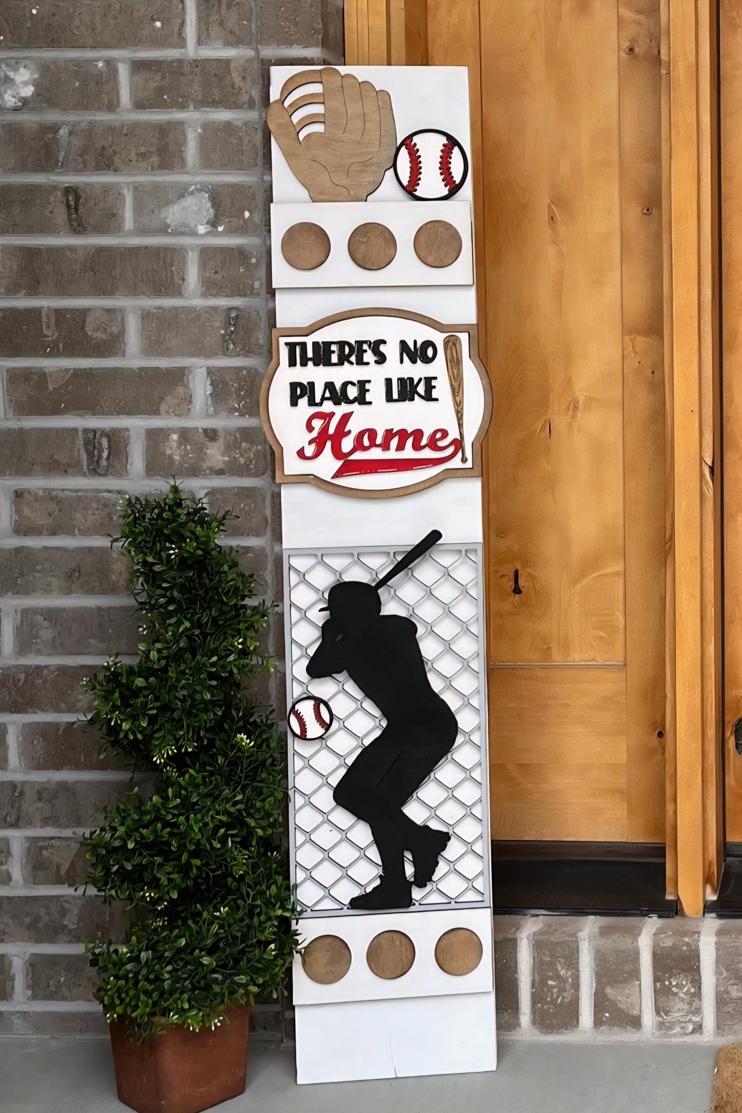 Baseball-themed decorative sign with 'There's No Place Like Home' text, placed against a brick wall.