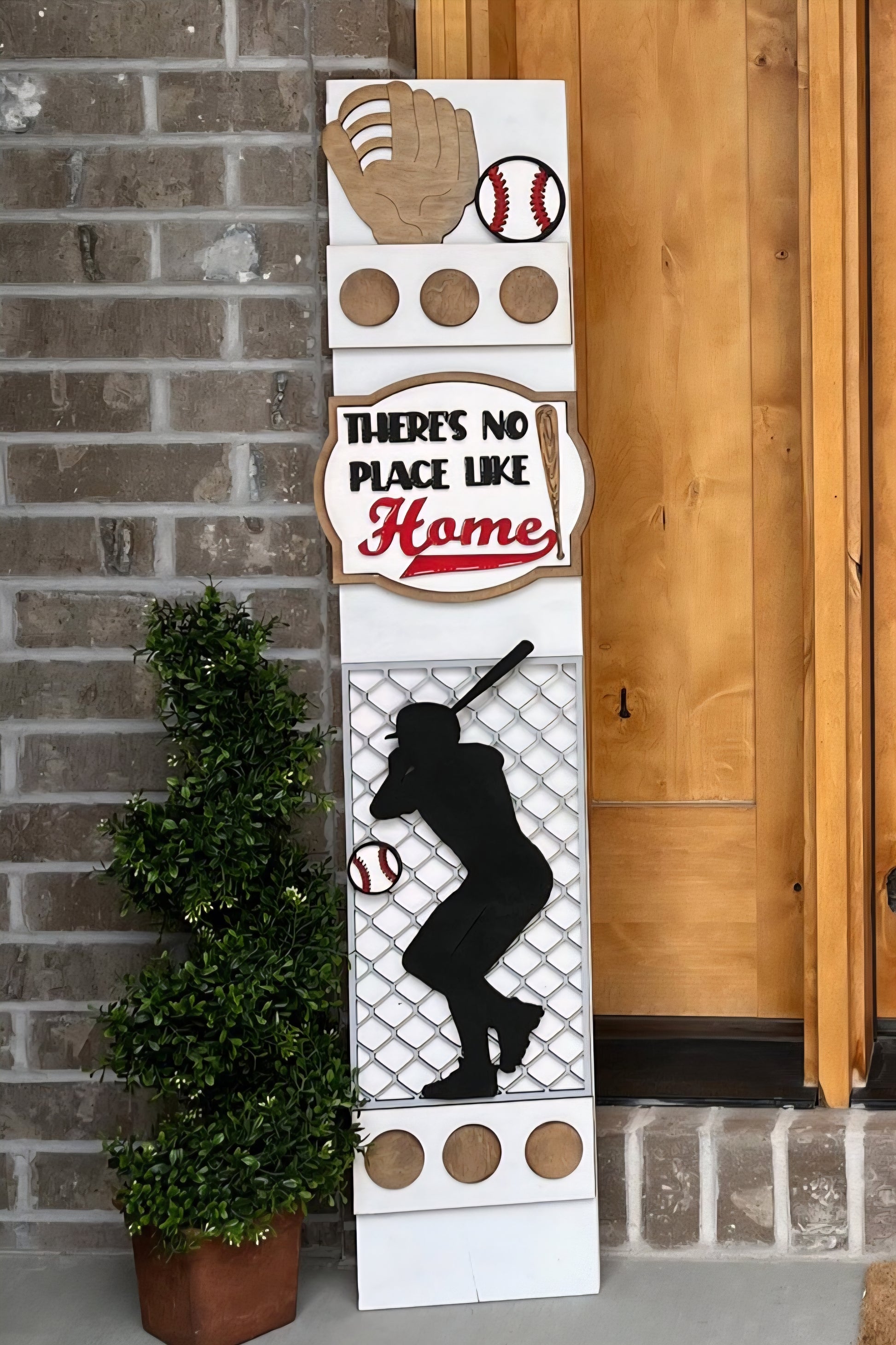 Baseball-themed decorative sign with 'There's No Place Like Home' text, placed against a brick wall.