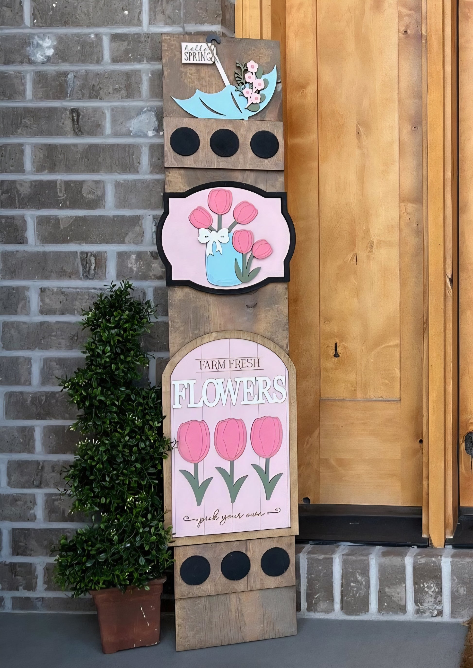 Decorative wooden sign with floral designs against a brick wall.