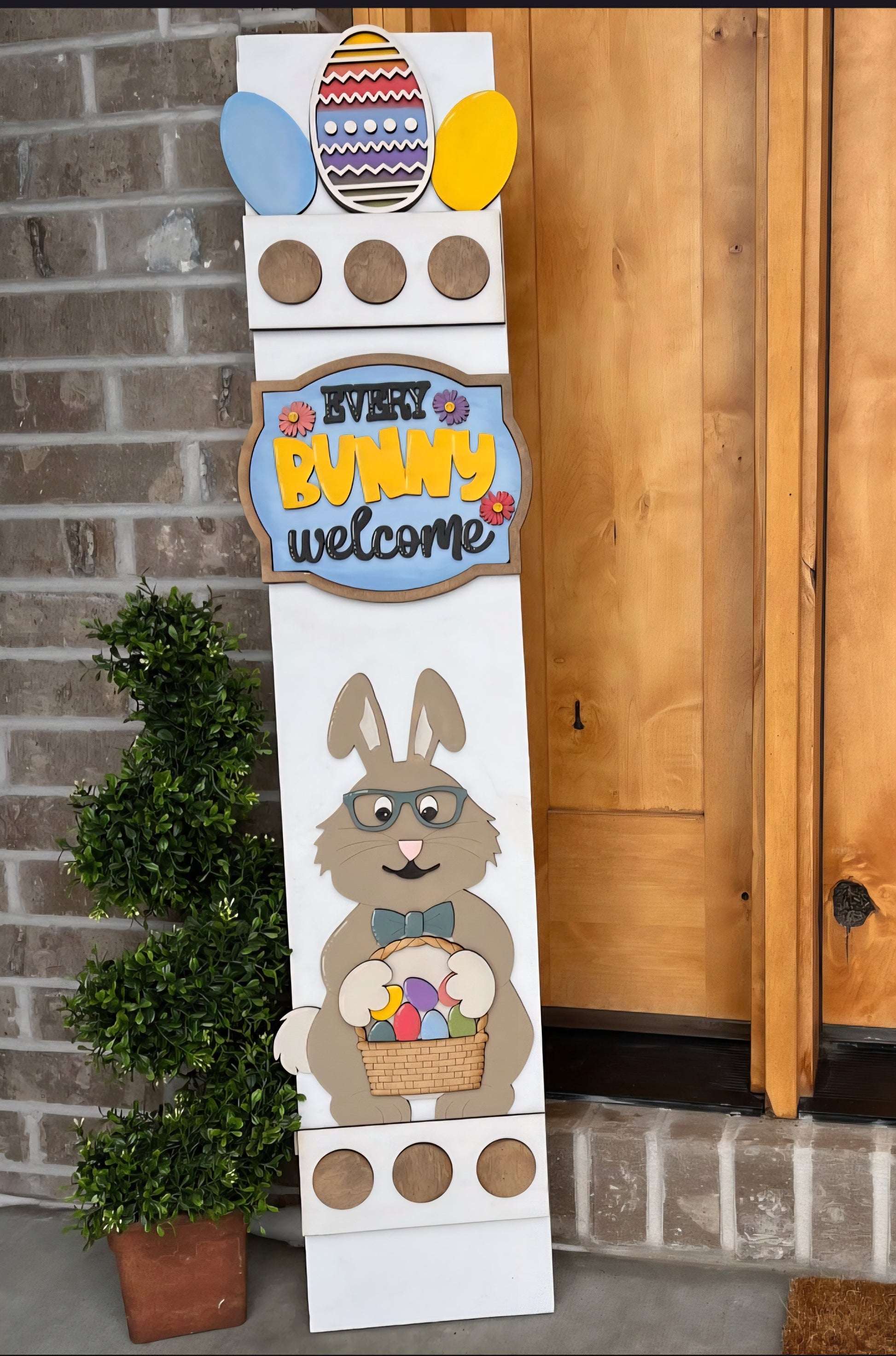 Decorative Easter sign with a bunny and eggs against a brick wall and wooden door background.