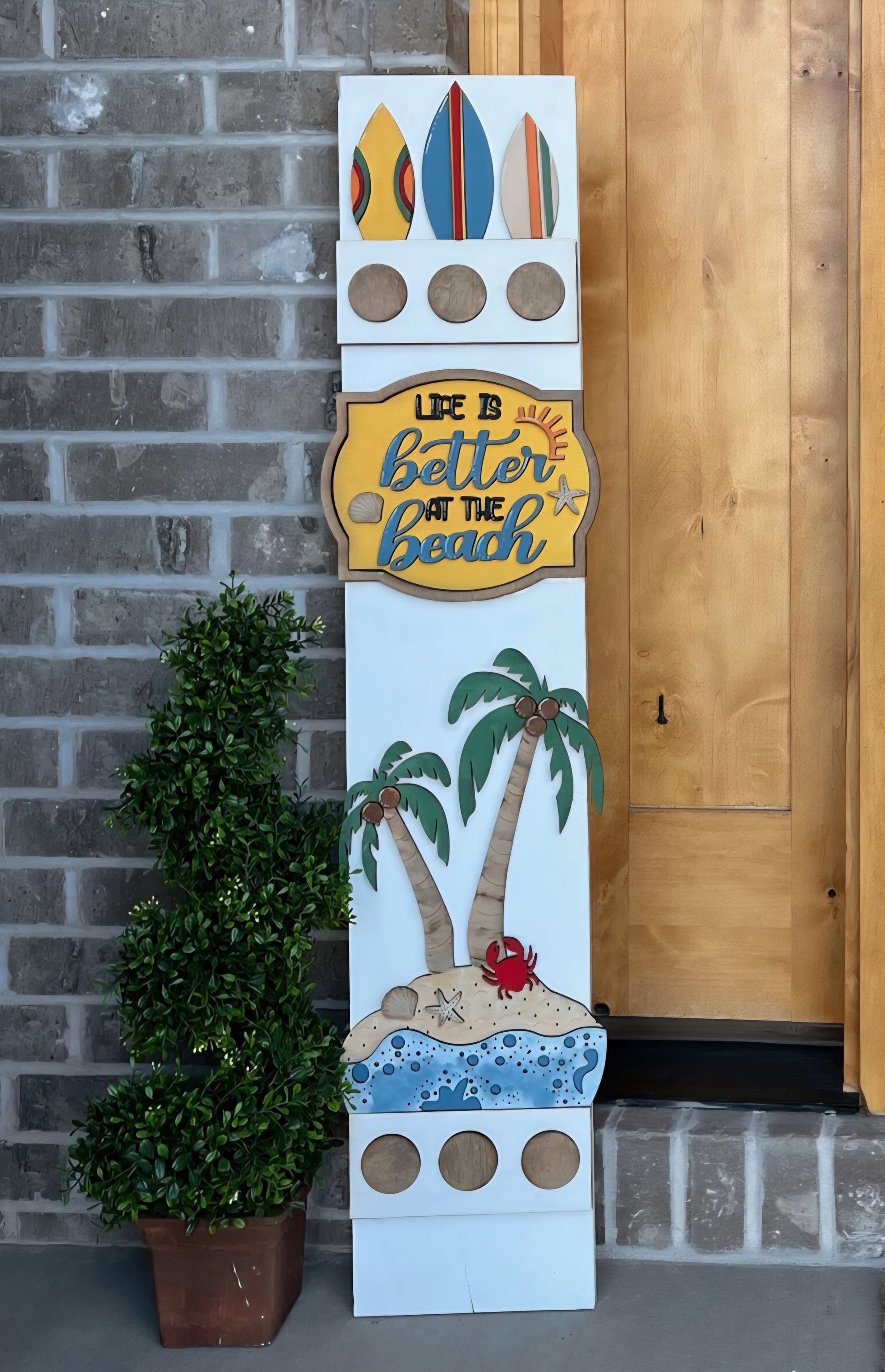 Decorative sign with beach theme and 'Life is better at the beach' text against a brick wall.