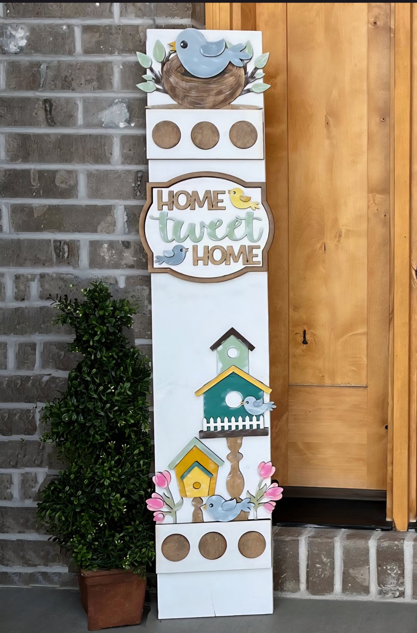 Decorative sign with birdhouses and 'Home Tweet Home' text against a brick wall.