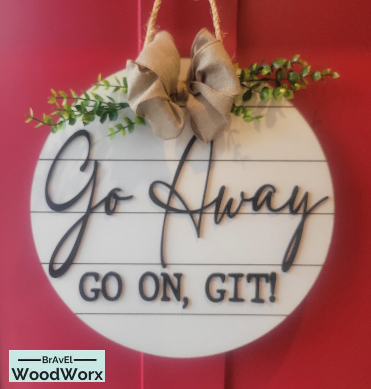 A round wooden door sign with a 'Go Away' message in bold script, decorated with a burlap bow and greenery.
